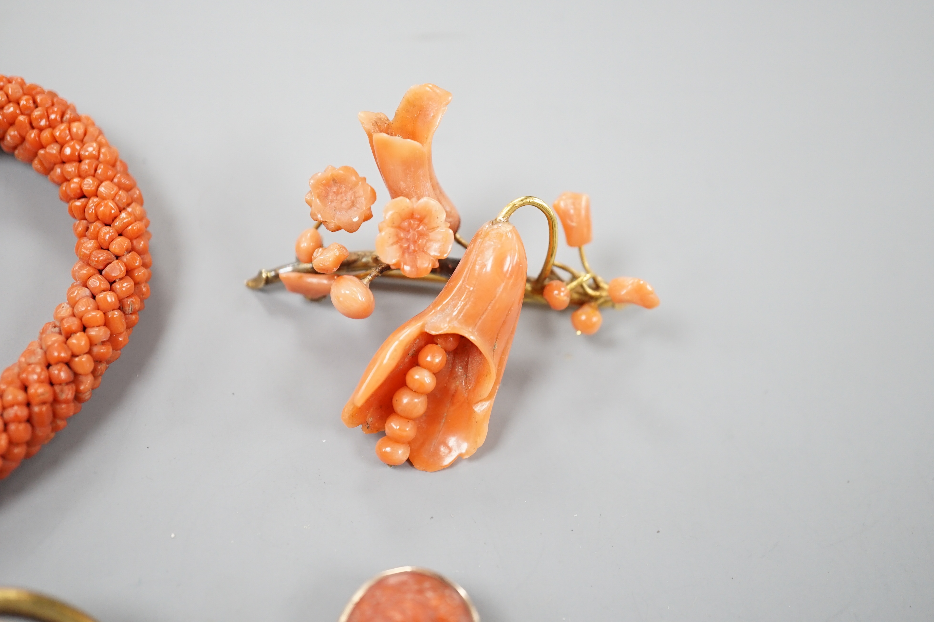 A yellow metal mounted carved coral oval brooch, 30mm, a mounted coral open bangle, a coral brooch and a gilt metal and enamelled brooch.